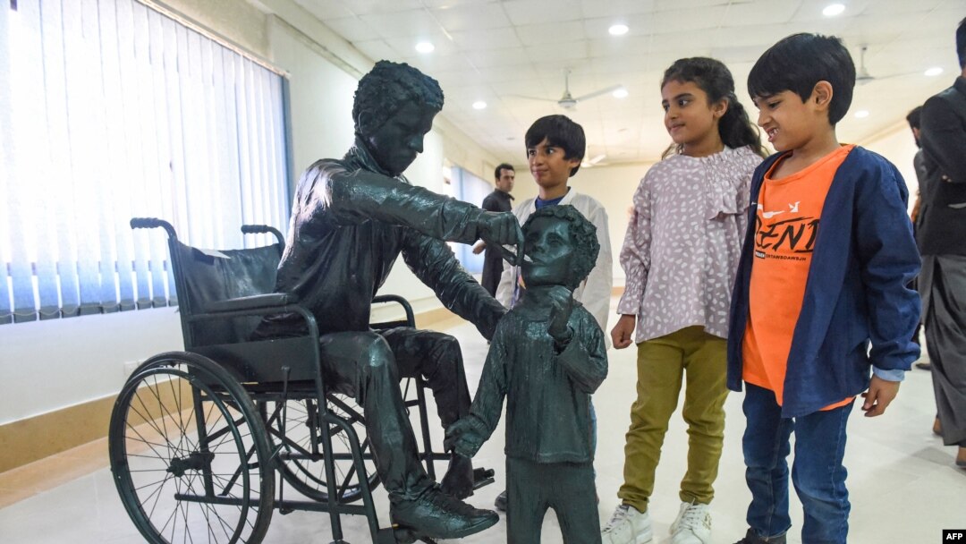 ماشومان د کوټې په یو پوهنتون کې هغې مجسمې ته ګوري چې پکې یو پولیو وهلی کس ماشوم ته د ګوزڼ واکسیني څاڅکي ورکوي - پخوانی انځور.