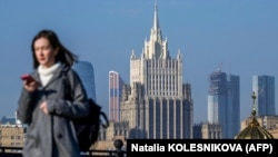 RUSSIA -- A woman looks at her phone as she walks across a bridge with the Russian Foreign Ministry building in the background, in central Moscow, on October 12, 2021.