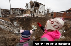 Діти дивляться на воронку, яка залишилася внаслідок російського ракетного удару, 2023 року