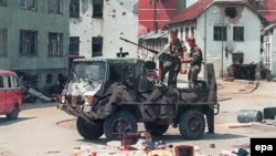 На снимке, датированном 16 июля 1995 года, бойцы боснийских сербов, проезжающие по пустым улицам Сребреницы после того, как войска Ратко Младича за неделю до этого вторглись в «безопасную зону» ООН.