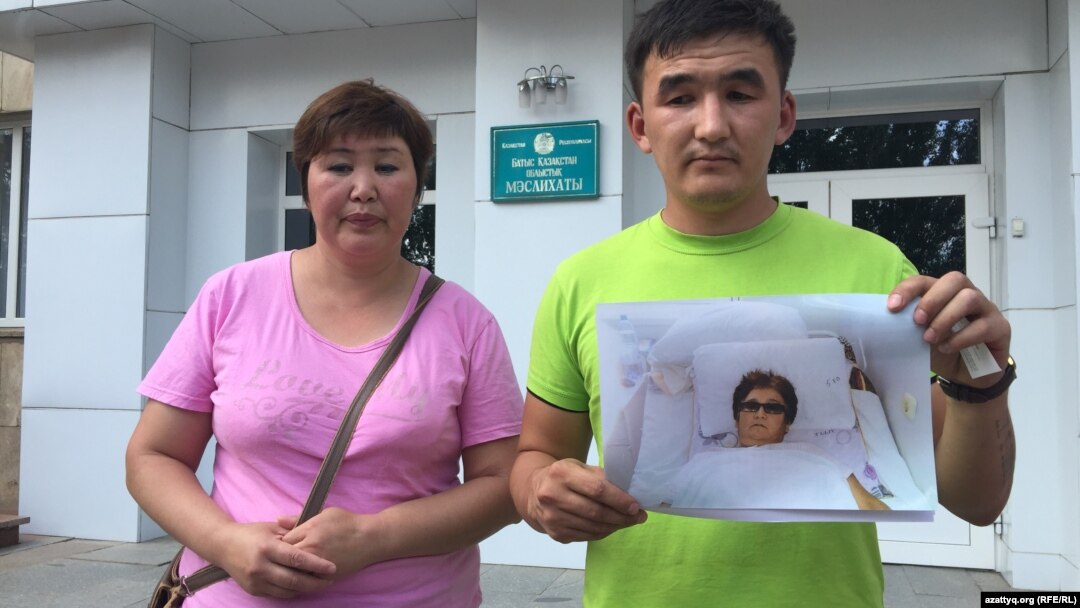 Житель Уральска Азамат Нурумов (справа) с фотографией своей матери стоит у здания областного управления здравоохранения, требуя привлечь к ответу врачей, которые, по его словам, отнеслись к работе халатно. Уральск, 14 июля 2015 года.
