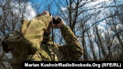 Український військовий дивиться в бінокль на позиції бойовиків на Донбасі